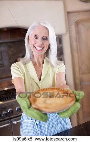 Stock Photography - Older woman holding pie in kitchen. Fotosearch