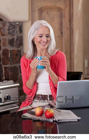 Stock Image - Older woman using laptop at breakfast. Fotosearch