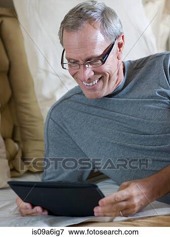 Older woman using tablet computer on bed View Large Photo Image Stock Photo - Older woman using tablet computer on bed. Fotosearch