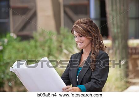 Picture - Realtor holding blueprints outside house. Fotosearch