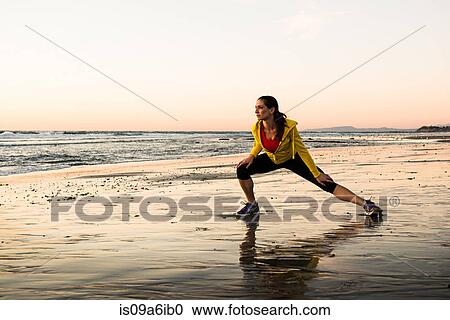 Stock Image - Runner stretching on beach. Fotosearch