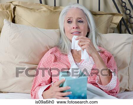 Stock Image - Sick older woman laying in bed. Fotosearch
