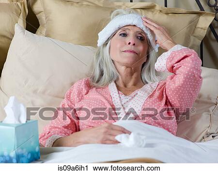 Stock Image - Sick older woman laying in bed. Fotosearch