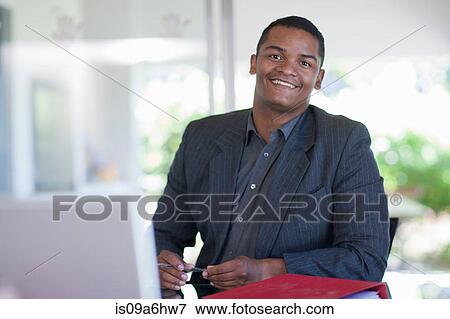 Stock Photo - Smiling businessman sitting at desk. Fotosearch
