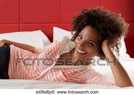 Stock Image - Smiling woman laying on bed. Fotosearch