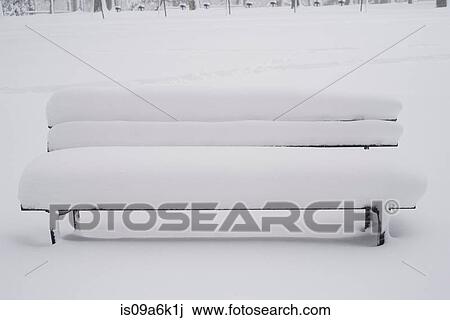 Stock Image - Snow covered bench in park. Fotosearch