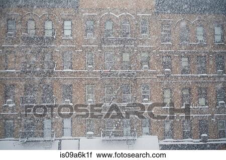 Stock Image - Snow falling by apartment buildings. Fotosearch
