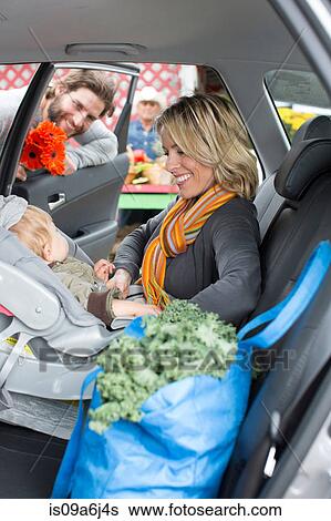 Stock Photograph - Woman buckling son in car seat. Fotosearch