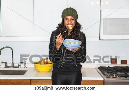 Woman eating fruit in kitchen View Large Photo Image Stock Photo - Woman eating fruit in kitchen. Fotosearch