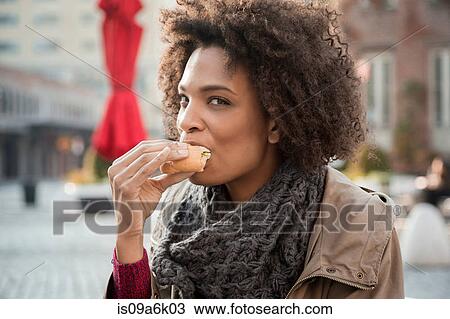 Stock Image - Woman eating on city street. Fotosearch