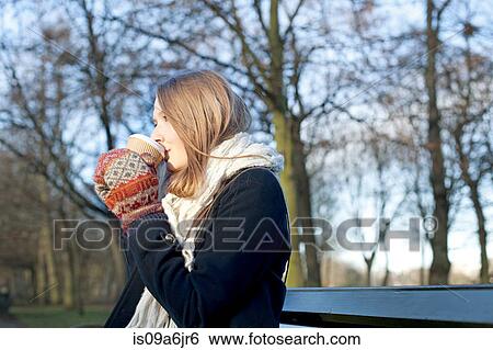 Stock Photograph - Woman having coffee on park bench. Fotosearch