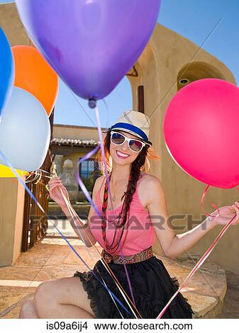 Picture - Woman holding bunch of balloons outdoors. Fotosearch