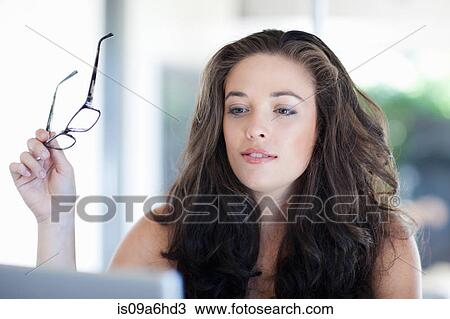 Stock Image - Woman holding glasses at desk. Fotosearch