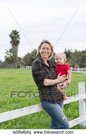 Stock Photography - Woman holding son by wooden fence. Fotosearch