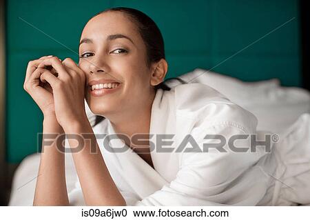 Stock Image - Woman in bathrobe smiling on bed. Fotosearch