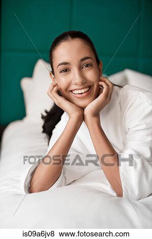 Stock Photo - Woman in bathrobe smiling on bed. Fotosearch