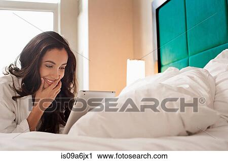 Stock Image - Woman in bathrobe using tablet computer. Fotosearch