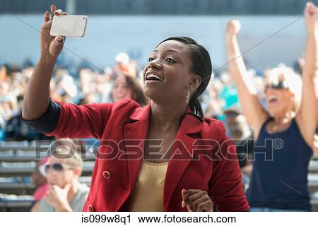 Stock Image - Woman in stadium, recording event with her phone. Fotosearch