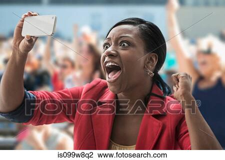 Stock Image - Woman in stadium, recording event with her phone. Fotosearch