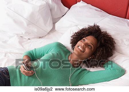 Woman listening to earphones on bed View Large Photo Image Stock Image - Woman listening to earphones on bed. Fotosearch