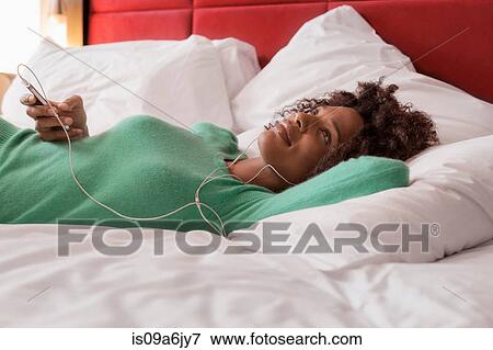 Stock Photo - Woman listening to earphones on bed. Fotosearch