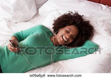 Stock Photograph - Woman listening to earphones on bed. Fotosearch