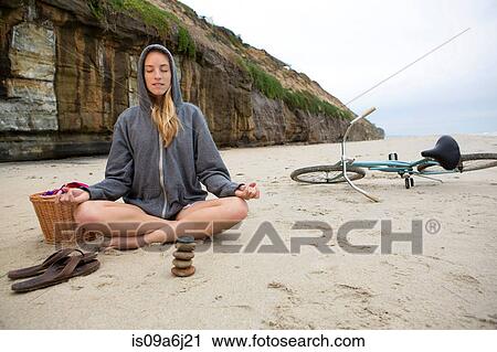 Stock Image - Woman meditating with rocks on beach. Fotosearch