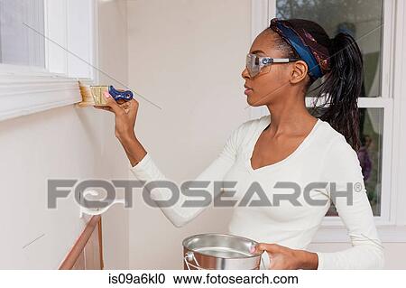Stock Image - Woman painting trimming in new home. Fotosearch