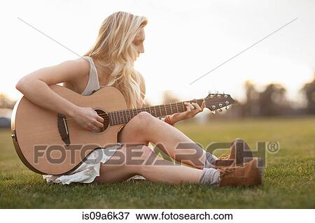 Stock Photo - Woman playing guitar in grass. Fotosearch