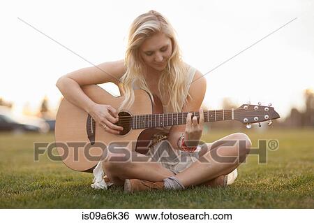 Stock Photograph - Woman playing guitar in grass. Fotosearch