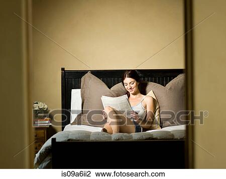 Stock Image - Woman reading newspaper in bed. Fotosearch