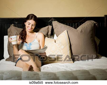 Stock Photography - Woman reading newspaper in bed. Fotosearch