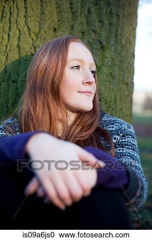 Stock Image - Woman sitting by tree outdoors. Fotosearch