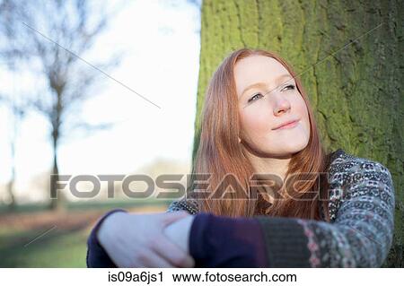 Stock Image - Woman sitting by tree outdoors. Fotosearch