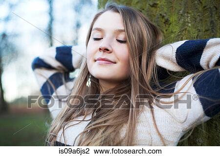 Stock Image - Woman sitting by tree outdoors. Fotosearch