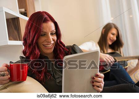 Stock Image - Woman using tablet computer on sofa. Fotosearch