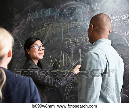 Woman writing on blackboard, colleagues watching View Large Photo Image Picture - Woman writing on blackboard, colleagues watching. Fotosearch
