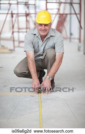 Stock Image - Builder measuring floor space on construction site. Fotosearch