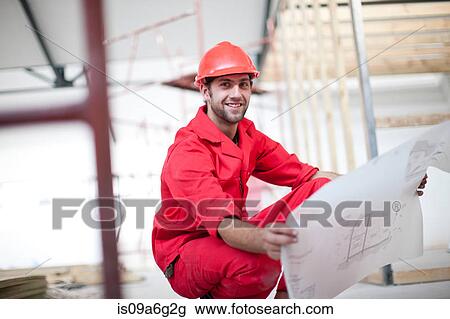 Stock Image - Builder with blue print on construction site. Fotosearch