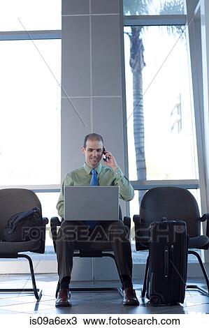 Stock Image - Businessman on cell phone using laptop. Fotosearch