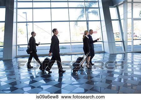 Stock Photo - Businesspeople walking through airport with suitcases. Fotosearch