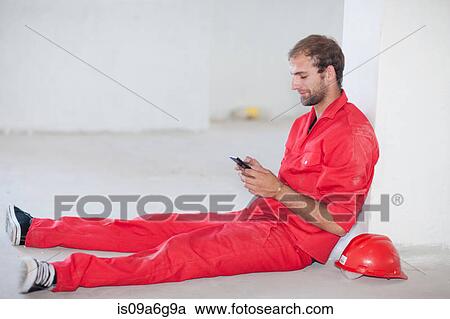 Stock Image - Construction worker sitting on floor taking a break. Fotosearch