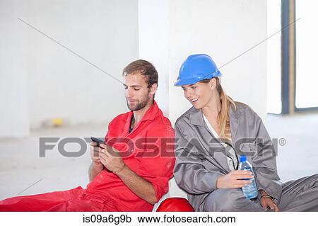 Stock Image - Construction workers sitting on floor taking a break. Fotosearch
