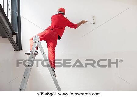 Stock Image - Decorator straddling step ladder. Fotosearch