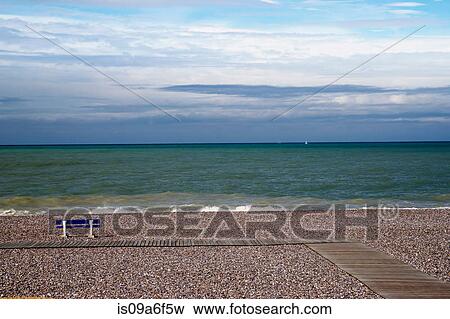 Stock Photo - Empty bench on shingle beach. Fotosearch