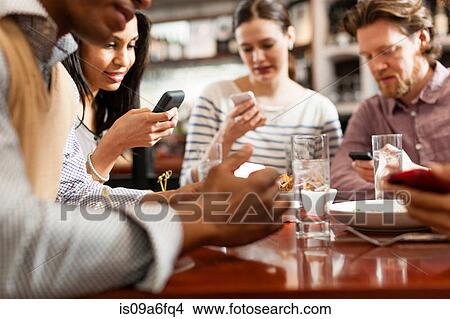 Picture - Friends at restaurant texting and showing photos using cell phones. Fotosearch