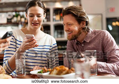 Stock Image - Friends at restaurant texting and showing photos using cell phones. Fotosearch