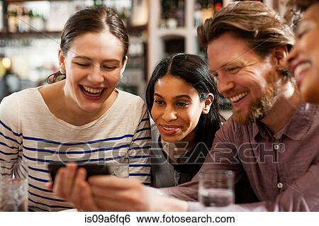 Friends at restaurant texting and showing photos using cell phones View Large Photo Image Stock Photograph - Friends at restaurant texting and showing photos using cell phones. Fotosearch