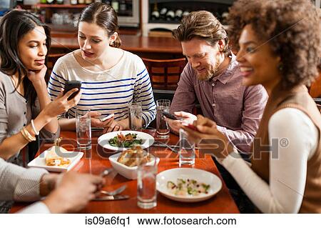 Stock Photography of Friends at restaurant texting and 