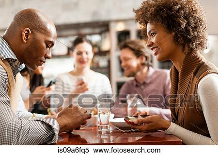 Friends at restaurant texting and showing photos using cell phones View Large Photo Image Stock Photography - Friends at restaurant texting and showing photos using cell phones. Fotosearch